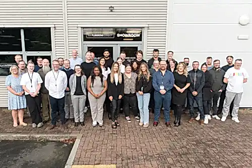 A large group of the UK Flooring Direct staff stood across the door of the Coventry showroom looking towards the camera